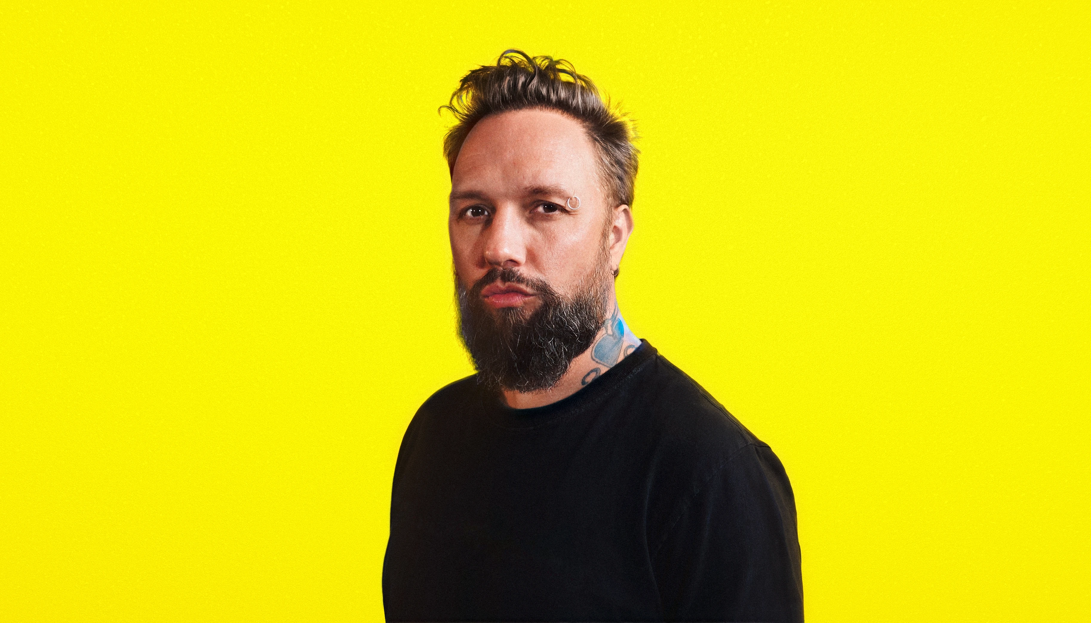 Akira The Don in a blank black shirt against a yellow background